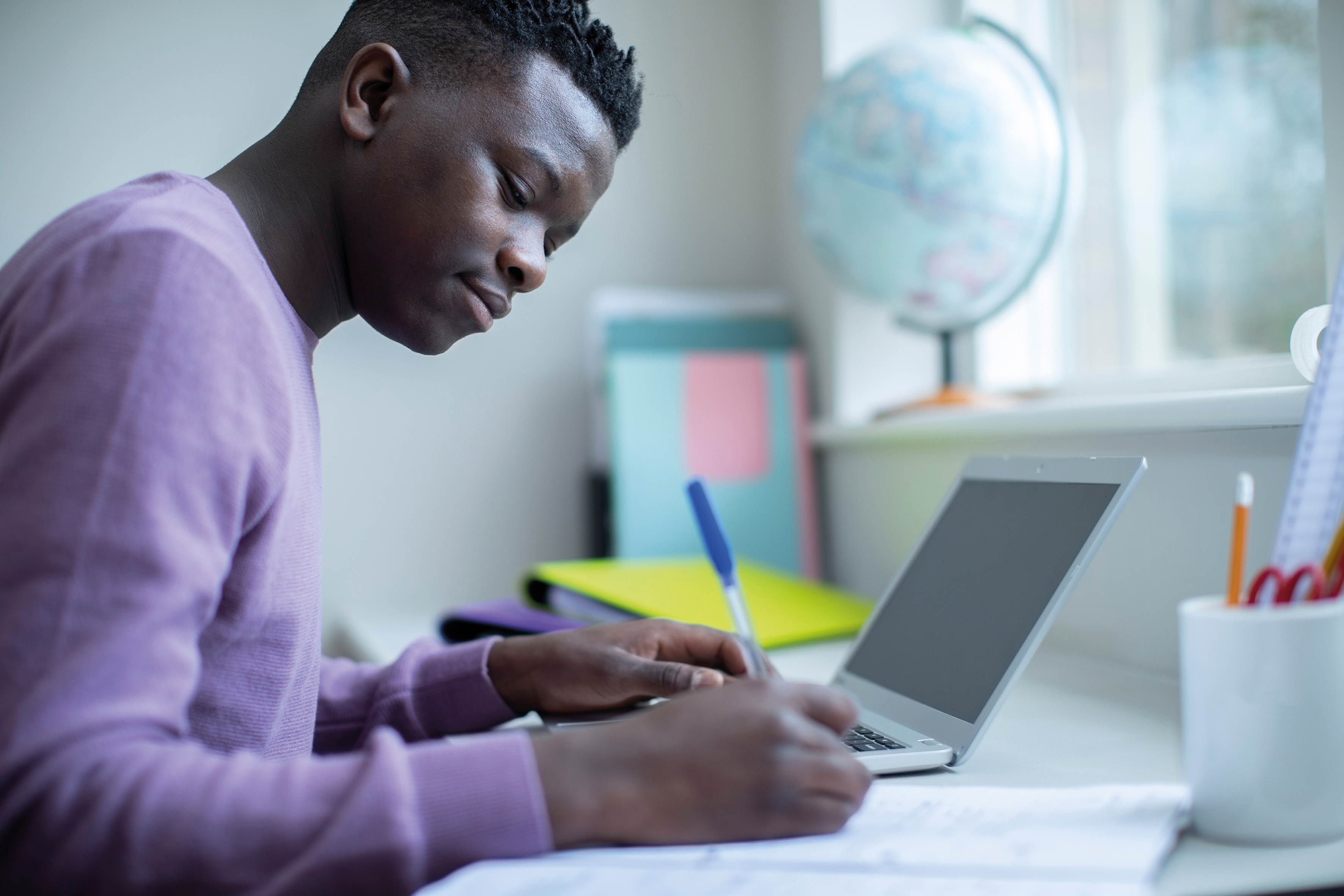 Man writing notes next to an open laptop